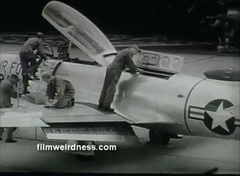 The still depicts a group of Air Force personnel working on a military aircraft, possibly a jet, from the 1950s. They are engaged in maintenance activities, with one individual accessing the cockpit. The plane features the U.S. Air Force insignia, highlighting its military context. The scene conveys a sense of teamwork and technical expertise in aviation.