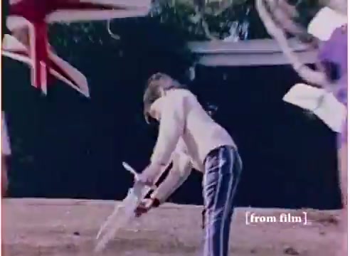 The still from the 16mm film features a child playing with a 'flying submarine' toy, set against a backyard backdrop. The child is dressed in light-colored clothing and appears to be engaged in an imaginative activity, possibly pretending to pilot the toy. Colorful elements, possibly other toys or decorations, are blurred in the background, enhancing the playful, whimsical atmosphere. The film lab paperwork dates back to 1972, indicating its vintage origin. The soundtrack has a designated 'good' version, contrasting with another version labeled 'DO NOT USE.'