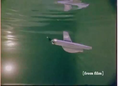 The still depicts a 'flying submarine' toy from a commercial produced by Goodtone, likely dating back to 1972. The toy is shown gliding through water, reflecting a playful and imaginative design that blends elements of both aviation and underwater exploration. The vibrant colors and underwater setting highlight the toy's unique concept, appealing to children's adventurous spirits. The film captures a nostalgic charm associated with toys of that era.