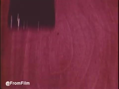 The still from the 'Flecto Varathane commercial - 1970s' features a paintbrush applying a glossy finish to wood, highlighting the product's effectiveness. The rich colors and textures showcase the product's quality. The 16mm print adds a nostalgic feel, characteristic of that era's advertisements. .