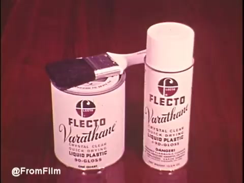 The still features a Flecto Varathane product display from the 1970s, showcasing a can labeled 'Flecto Varathane' alongside an aerosol spray can. A paintbrush rests on the open can, emphasizing the product's application. The design reflects the era's aesthetic with bold typography and a vibrant background, highlighting the brand's focus on liquid plastic finishes. Follow @FromFilm for more vintage content!