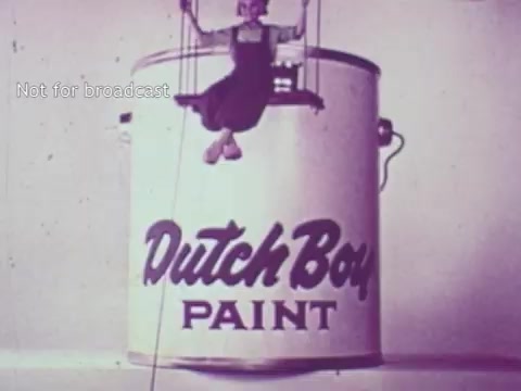 The 16mm still depicts a whimsical scene from a 1970s Dutch Boy Paint commercial. A character, depicted in a playful and artistic style, is seen sitting on the rim of a large paint can labeled 'Dutch Boy PAINT.' The visual reflects the upbeat and creative advertising approach typical of the era, emphasizing the brand's playful identity. The overall aesthetic is vintage, with soft colors characteristic of the time period.