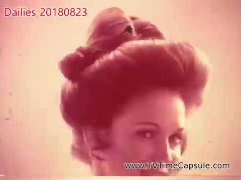 The still captures a woman with an elegant, styled updo that emphasizes vintage fashion. The image has a soft, warm tint, suggesting a nostalgic or retro aesthetic. The woman's expression appears playful and confident, adding to the overall charm of the scene.