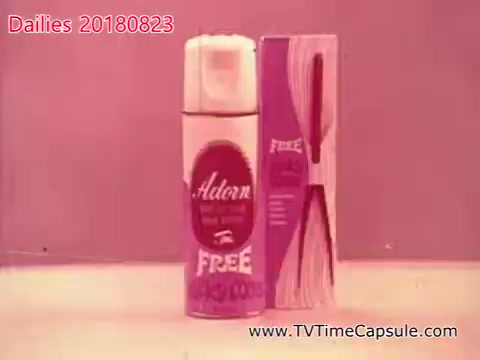 The still features a can of 'Adorn' spray alongside a pack of towels, both presented against a soft, pink background. The can is prominently labeled with 'FREE' in bold, suggesting a promotional offer. The imagery appears to be from a vintage advertisement, emphasizing the product's appeal in a retro aesthetic.