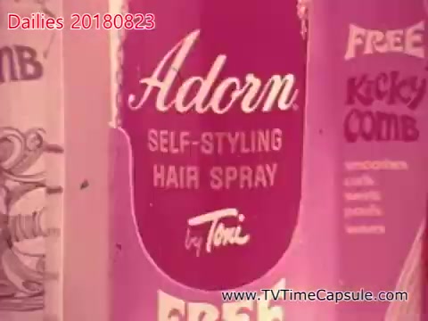 The still features a vintage product advertisement for 'Adorn Self-Styling Hair Spray' by Toni. The design is predominantly pink, highlighting the brand name and product benefits, indicative of mid-20th century marketing aesthetics. There are also references to promotional items, such as a 'Free Kick Comb,' suggesting a focus on product appeal to consumers during that era.
