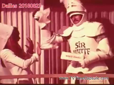 The still features a humorous scene with a character dressed as a knight labeled 'Sir White' engaging with a woman, who appears surprised or playful. The knight is holding a towel and seems to be presenting it, while the woman gestures in reaction. The setting has a lighthearted, comedic tone typical of skits or performances. The color tone suggests a vintage or retro aesthetic.
