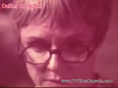 The still from 'dailies 20180823-scott-towels-etc' shows a close-up of a woman wearing glasses, focused intently on something out of frame. The image has a reddish hue, suggesting it may be from a film with a vintage or artistic style. The overall mood appears contemplative or serious.
