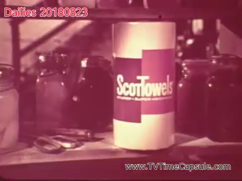 The still features a canister of ScotTowels prominently displayed on a table or countertop. Surrounding the canister are various jars, suggesting a setting related to home or food preparation. The overall aesthetic has a vintage feel, indicative of a specific time period, likely captured during film dailies.