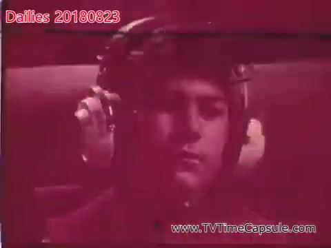 The still features a young man with headphones on, appearing focused or contemplative. The lighting has a reddish tint, suggesting a dramatic or stylistic aesthetic. The context seems to relate to audio or sound recording, likely from a film or television production, as indicated by the label 'dailies.'