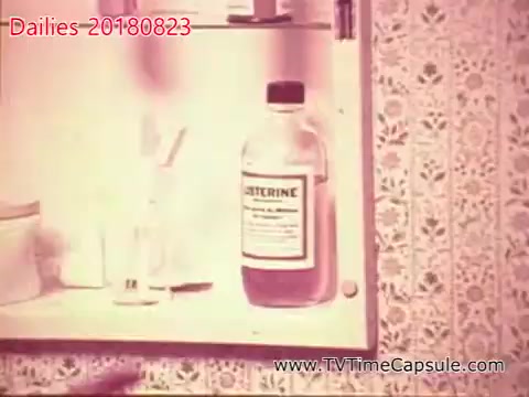 The still features a bathroom cabinet with vintage decor, displaying a bottle of Listerine prominently. The background features patterned wallpaper, suggesting a mid-20th century aesthetic. The image reflects everyday domestic life, emphasizing personal care products.