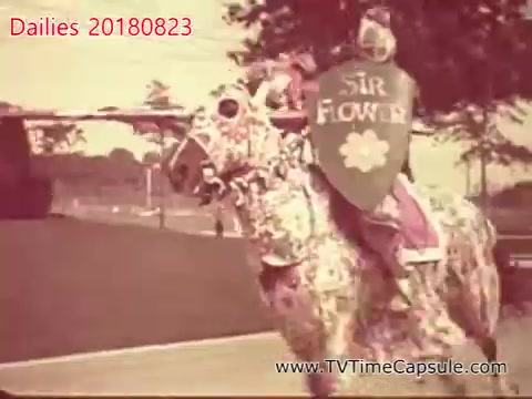 The still features a costumed individual riding a horse adorned in a floral pattern, carrying a shield that reads 'Sir Flower.' The scene appears to be playful and whimsical, likely intended for entertainment or a themed event. The vintage 16mm quality adds a nostalgic feel to the image.
