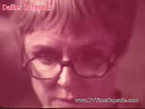 The still shows a close-up of a woman with short hair and glasses, displaying a focused expression. The image has a vintage look, characteristic of 16mm film, with warm color tones. The context appears to involve behind-the-scenes footage or a candid moment captured during the day.