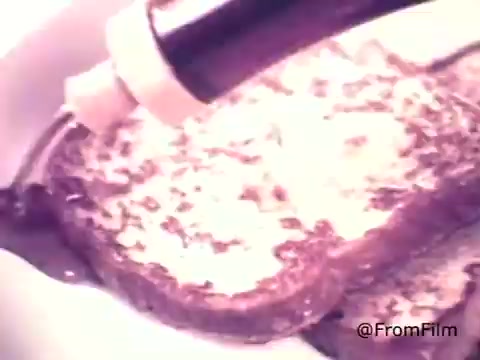 The still from 'Golden Griddle Pancake Syrup - 1970's' depicts a close-up shot of syrup being poured onto slices of French toast. The syrup has a rich, glossy appearance, and the scene exudes a warm, inviting ambiance characteristic of 1970s food advertising. The color palette has a nostalgic feel, typical of the era’s aesthetic. The focus on the syrup suggests indulgence and highlights the product's appeal.   .