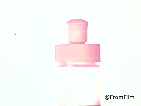 The still from the 1970s advertisement for Golden Griddle Pancake Syrup features a close-up of a syrup bottle, prominently showcasing its cap. The background is highly illuminated, possibly creating a soft, dreamy effect around the product. The overall aesthetic reflects the vintage style typical of that era's advertisements, emphasizing simplicity and focus on the product.