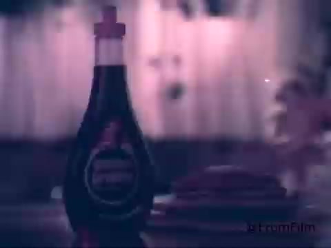 The still features a bottle of Golden Griddle Pancake Syrup prominently displayed in the foreground, with a stack of pancakes in the background. The scene has a nostalgic, slightly muted color palette characteristic of 1970s film stock. Soft focus and diffused lighting contribute to the warm, inviting atmosphere typical of breakfast commercials from that era. The composition highlights the syrup as a key ingredient for a comforting breakfast.