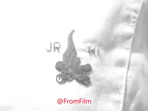 The still shows a close-up of a fabric patch featuring a stylized emblem, likely related to a youth organization, with the letters 'JR' and a design resembling a flame or fire motif. The image appears somewhat distorted or warped. The overall tone is reminiscent of 1969, reflective of the camp-themed context of the PSA.