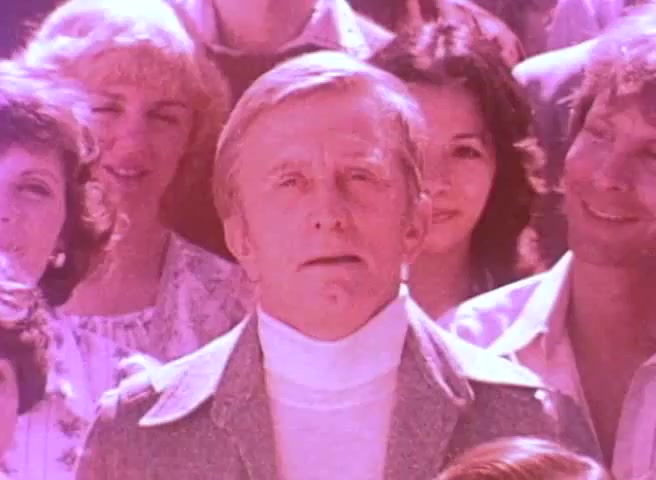 The still features Kirk Douglas prominently in the foreground, wearing a turtleneck beneath a jacket, with a serious expression. He is surrounded by a diverse group of people in the background, some smiling, highlighting a community theme. The overall visual has a vintage 16mm film quality, with soft colors typical of that era, emphasizing the importance of the 1980 Census message.