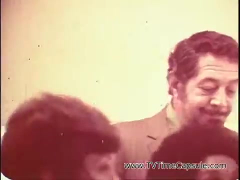 The still from 'Lasting Beauty makeup finish - 1969' captures a moment with David Lawrence, a makeup artist known for his work in film and television. He is likely demonstrating a makeup application technique, inviting viewers—specifically women—to close their eyes as he prepares to showcase the Lasting Beauty makeup finish. The overall atmosphere seems light and instructional, reflecting his long-standing experience in helping women enhance their beauty. The image likely features David in a relaxed setting, engaging with his audience.