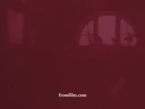 The still from the 'Gravy Train Dog Food Commercial' features a muted, reddish hue typical of a 16mm print, suggesting age or color degradation. The image appears to portray an interior space, with vague silhouettes visible through a window, hinting at a domestic setting. The overall mood is nostalgic, reflecting the visual style of mid-20th century advertising.