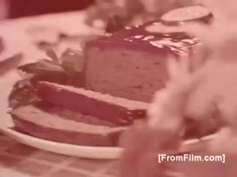 The 16mm still from 'Betty Crocker Julienne Potatoes - 1970s' features a visually appealing presentation of a meatloaf alongside sliced julienne potatoes, garnished with leafy greens. The colors exhibit a warm, nostalgic tone characteristic of the era, highlighting the home-cooked meal aesthetic. The setting suggests a family dining experience, typical of 1970s culinary advertising.