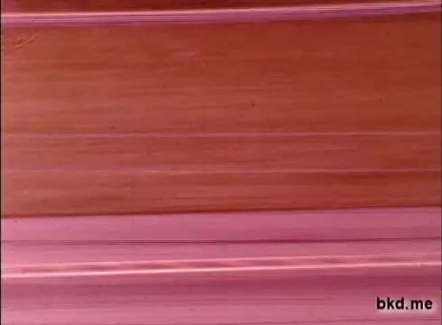 The still appears to be a frame from 16mm footage, likely capturing the early laps of a practice session at the Indianapolis Motor Speedway during the late 1960s. The image features a blurred view of the track, characterized by lines of color suggesting motion, possibly from racing cars. The overall aesthetic reflects the vintage quality of early motorsport cinematography, creating a nostalgic glimpse into the era of Al Unser and Mario Andretti's racing careers.