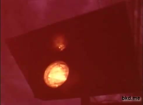 The 16mm still appears to focus on a dimly lit traffic signal, likely displaying a red light, indicative of a stop or caution. The color tone suggests it was filmed in low light, possibly during early evening or under cloudy conditions. This footage seems to reflect a moment from a practice session at the Indianapolis Motor Speedway, possibly from the late 1960s, capturing the atmosphere of racing before the Indy 500. The graininess typical of 16mm film adds to its vintage aesthetic.