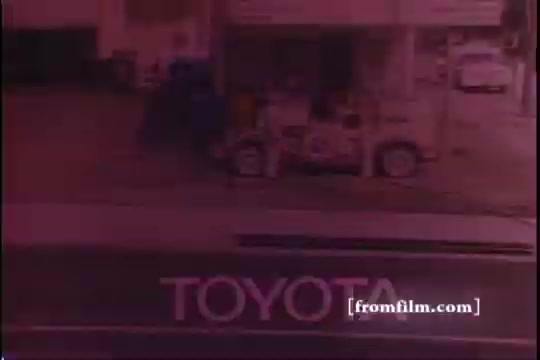 The still features a vintage 16mm frame from a 1970s Toyota commercial, showcasing the Toyota Celica GT. In the background, there's evidence of a gas station, adding to the nostalgic atmosphere. The image has some sprocket damage, indicating its age and wear over time. The prominent “TOYOTA” logo is clearly visible in the foreground.