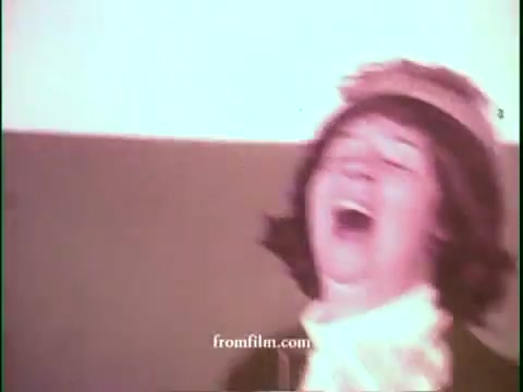 The still from the 16mm print of the 'United Airlines - Deal of the Century' commercial features a performer wearing a playful costume, laughing joyfully. The overall color tone appears warm and slightly faded, characteristic of 1970s film stock. This game show commercial likely promotes excitement around United Airlines’ offers, capturing the playful and vibrant spirit of the era.