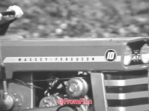 The still from the Massey Ferguson lawn tractor commercial featuring Jerry Colonna showcases a close-up of the tractor's hood with the 'MASSEY-FERGUSON' branding prominently displayed. The tractor is marked with a distinctive '10,' indicating its model. The design highlights the industrial aesthetic typical of the 1960s. The background appears blurred, focusing the viewer’s attention on the tractor itself, conveying a sense of reliability and strength associated with the brand.   For project licensing or higher resolution options, please reach out for further details.