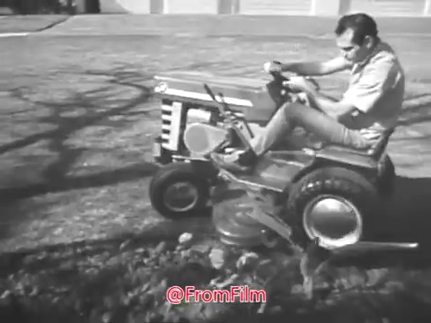 The still from the Massey Ferguson lawn tractor commercial features a man operating a lawn tractor. He appears focused on the task at hand, showcasing the tractor's functionality in a yard setting. The scene is in black and white, typical of 1960s commercials, and captures the essence of suburban gardening and the appeal of using machinery for lawn care. The overall presentation emphasizes efficiency and practicality for homeowners.
