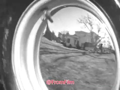 The still from the Massey Ferguson Lawn Tractor commercial featuring Jerry Colonna likely showcases a reflective view from the wheel of the tractor. You can see the surrounding scenery, including grassy areas and possibly a house in the background, creating a nostalgic and rural atmosphere typical of 1960s advertisements. The black-and-white aesthetic enhances the vintage feel, highlighting both the product and the serene outdoor setting.