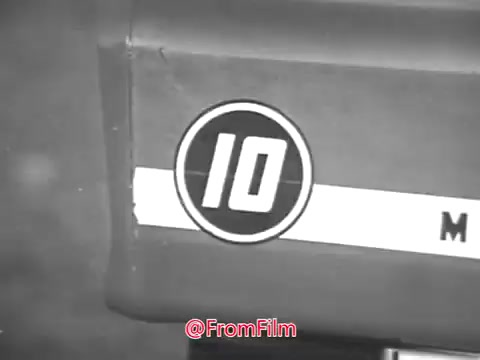 The still from the 1960s Massey Ferguson lawn tractor commercial features a close-up of the tractor, focusing on a circular emblem with the number '10' prominently displayed. The design is classic and simple, reflecting the era's advertising style. There’s a horizontal stripe across the tractor, likely part of the branding. This image encapsulates the promotional effort centered around the rugged reliability of Massey Ferguson products, as endorsed by Jerry Colonna. For licensing inquiries and higher resolution digital files, interested parties should reach out directly regarding options.
