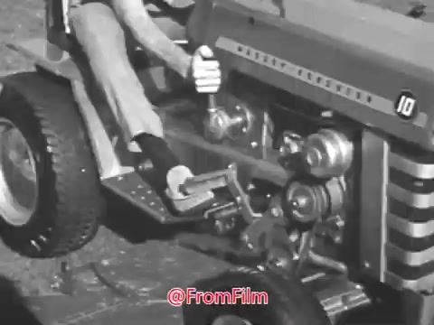 The still from the Massey Ferguson lawn tractor commercial featuring Jerry Colonna showcases a close-up of a person operating the tractor. The image highlights the controls and mechanical elements of the tractor, emphasizing its functionality. The commercial likely presents the mower as an approachable and efficient tool for lawn care in the 1960s. The overall aesthetic is characteristic of vintage advertising, combining practical demonstrations with a lighthearted touch associated with Colonna's persona.
