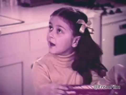 The still from the 'Baggies alligator storage bags' commercial features a young girl in a kitchen setting. She appears surprised or curious, wearing a light-colored sweater and a hair bow. The focus of the scene is on the product—Baggies alligator bags—which promise protection against freezer burn, as highlighted by a man's voiceover discussing their effectiveness. The warm, nostalgic color tone adds a retro charm to the advertisement.