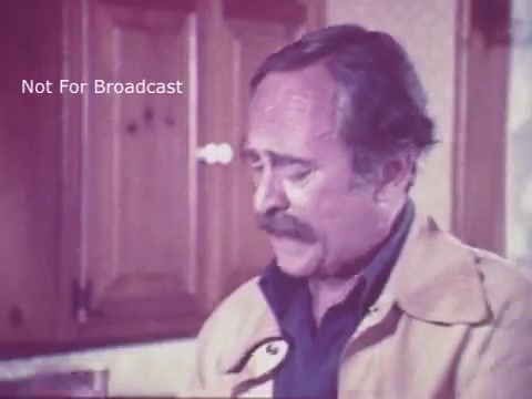 The still from the 16mm PSA titled 'Toy Safety' features a man with a mustache and a serious expression, potentially discussing toy safety issues. The setting appears to be a kitchen, with wooden cabinetry in the background, indicating a domestic environment. This Public Service Announcement likely aimed to educate viewers about toy safety regulations and the importance of ensuring toys are safe for children. The blue and beige color palette suggests a typical 1970s aesthetic. The 'Not For Broadcast' label indicates it is meant for educational or archival purposes, rather than commercial distribution.