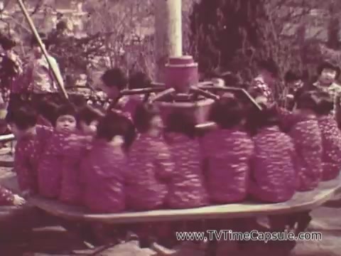 The still from the 'Christian Children's Fund PSA' depicts a group of children, all wearing matching outfits, joyfully playing on a roundabout in a playground setting. The scene conveys a sense of camaraderie and happiness as the children engage in play, likely emphasizing the theme of childhood and community support associated with the organization's mission. The background appears to have trees and other children, enhancing the atmosphere of a lively, outdoor environment.
