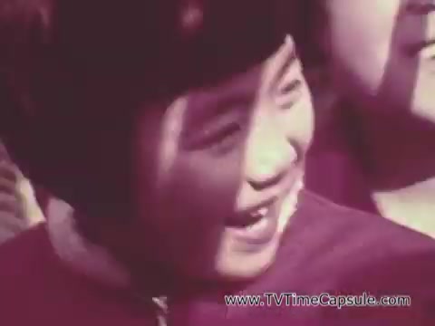 The still from the 'Christian Children's Fund PSA' features a young child with short hair, smiling joyfully. The child is wearing a maroon garment and is part of a group, suggesting a communal or supportive environment. The soft focus and warm tones evoke a sense of warmth and hope, typical of public service announcements aimed at promoting child welfare and humanitarian aid.