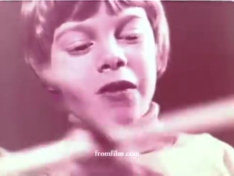 The still from the 'Muscular Dystrophy PSA: No Strings' features a young boy, likely playing or interacting with a prop, conveying a sense of joy or determination despite his condition. The image has a soft, pink hue, which suggests a nostalgic or emotional tone typical of PSAs from the early 1970s. The overall message aims to evoke sympathy and encourage viewers to donate, highlighting the impact of muscular dystrophy and the need for support.