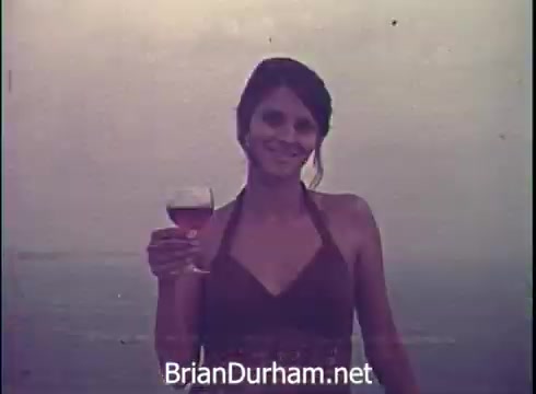 The still features a woman smiling while holding a glass of Lancer wine. She appears to be outdoors, possibly by a beach or water, with a soft, muted background. The overall ambiance suggests a relaxed and cheerful atmosphere typical of a vintage wine commercial from 1971.