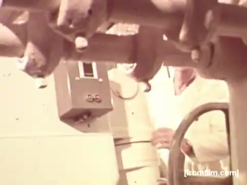 The 16mm still from the 'Pepperidge Farms - Apollo 17' commercial features a close-up of machinery in a production facility. In the background, individuals in white lab coats are engaged with the equipment, emphasizing a sterile and professional atmosphere. The absence of voiceover allows the visuals to focus on the processes involved in bread production, highlighting the brand's commitment to quality. The scene likely connects the idea of scientific precision with the heritage of their bread being part of space missions.