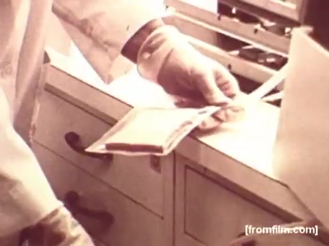 The 16mm still from the 'Pepperidge Farms - Apollo 17' commercial features a close-up of a gloved hand holding a package of bread. The setting appears to be a sterile environment, possibly a laboratory or food processing area, indicative of the brand’s connection to space missions. The image emphasizes precision and care in food preparation, aligning with the commercial's theme of quality and reliability associated with Pepperidge Farms products used in NASA missions.