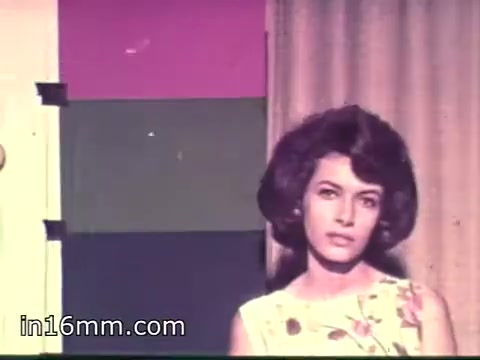 The still features a woman with a stylish 1960s hairstyle, wearing a floral dress. She appears to be posing or presenting in front of a colorful backdrop with blocks of color, likely intended to enhance the visual appeal. The setting suggests a promotional or recruiting context related to the Air Force Reserve, indicative of the era's marketing style.