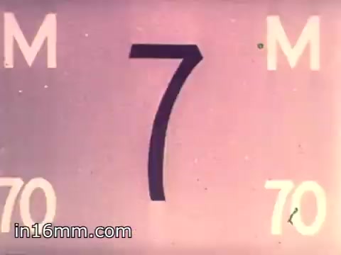 The still features a large, bold number '7' prominently displayed in the center against a light background. The surrounding graphic includes the letters 'M' and the number '70' on either side, indicating a focus on the concept of measurement or timing, likely related to the film's context in Air Force Reserve recruiting. The color palette is soft, with a vintage aesthetic typical of 1960s film.