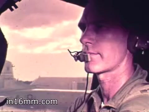 The still shows a male pilot in the cockpit of an aircraft, looking intently ahead. He is wearing a microphone headset and a flight suit, suggesting a professional military context. The background features a cloudy sky, indicating a flight environment. The image captures a moment of focus and dedication typical of Air Force Reserve crew members from 1968.