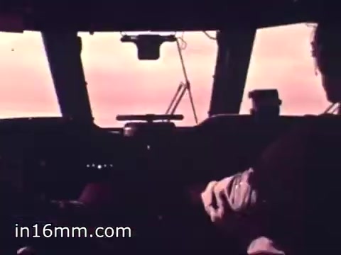 The still from 'Air Force Reserve Recruiting - 1968 - Air Crews' depicts the cockpit of an aircraft, likely during flight. The image captures a pilot, seated and focused, with controls and instruments visible in front of him. The view through the cockpit windows shows a hazy sky, suggesting either dawn or dusk. The overall tone conveys a sense of duty and adventure associated with Air Force operations.