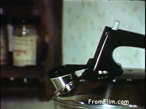 The still from the 'C and P Telephone commercial' features a close-up of a kettle with a distinct spout and handle, likely in a kitchen setting. The background suggests a typical domestic environment, with jars or containers visible on a shelf. This scene likely aims to convey a sense of everyday life, emphasizing how C&P Telephone connects families through communication. The vintage aesthetic aligns with the early 1970s, capturing the simplicity and familiarity of that era. Overall, it evokes a warm and relatable context for viewers.