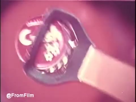 The still features a close-up of a bottle opener poised over a classic orange soda bottle cap, showcasing the iconic retro design typical of the 1970s. The colors are vibrant, reflecting the fun and energetic vibe of the era, likely emphasizing the refreshing nature of Orange Crush. Overall, it encapsulates the lively atmosphere of vintage soda commercials.   Follow us on Twitter @FromFilm.