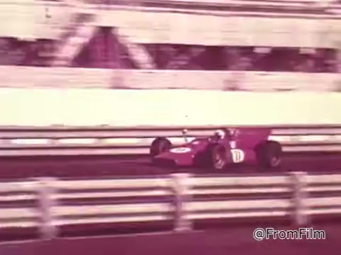 The still shows a vibrant red race car, driven by Roger McClusky, speeding along a racetrack. The background features blurred spectators and a grandstand, characteristic of 1960s motorsport events. The image captures the excitement and energy of racing, combined with the nostalgic aesthetic of a 16mm film print.