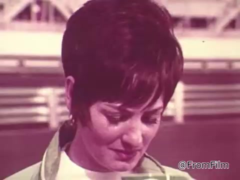 The still features a woman with short, stylish hair, looking down with a contemplative expression. She's likely in a race setting, which reflects the high-energy atmosphere of the 1960s. The color palette suggests a vintage aesthetic typical of the era. The context involves Roger McClusky and is centered around promoting Chase and Sandborn Coffee, aiming to connect the excitement of racing with the brand.