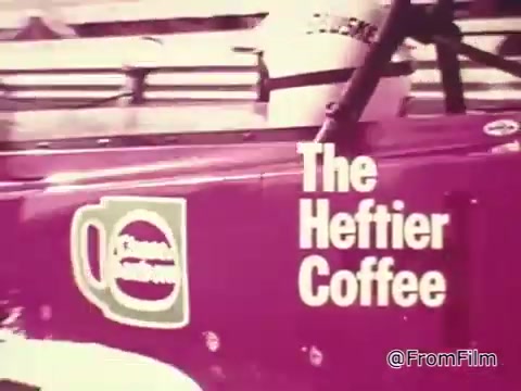 The still features a race car prominently displaying the 'Heffier Coffee' logo. The vehicle appears to be racing-themed, indicative of the 1960s era, with a vibrant color scheme. It captures a sense of speed and excitement, aligning with the promotional context of the Chase and Sandborn Coffee commercial featuring race car driver Roger McClusky. The overall appearance reflects the nostalgic design style of that time.